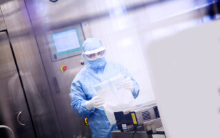 Symbiosis Pharmaceutical Services scientist wearing full PPE in a laboratory, holding equipment