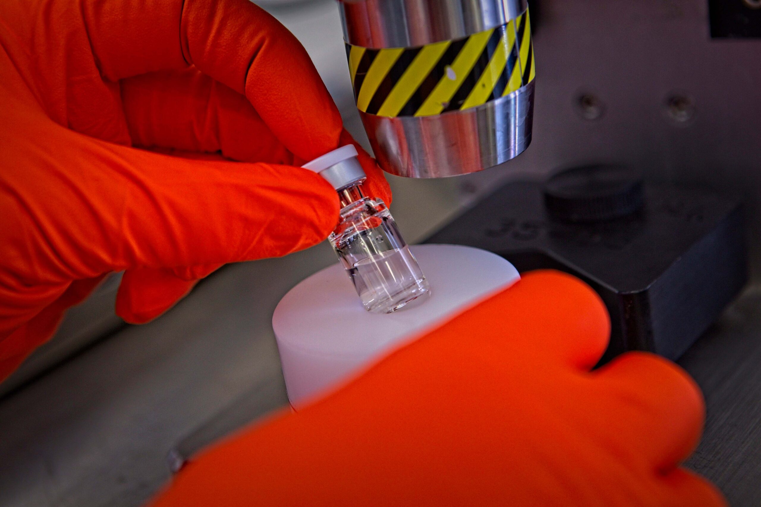 Gloved hands of a biologics CMO scientist removing a vial from the automatic crimper