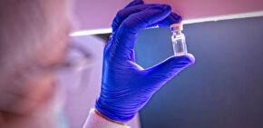 Gmp biologics manufacturing scientist holding a vial of drug product up to the light for visual inspection