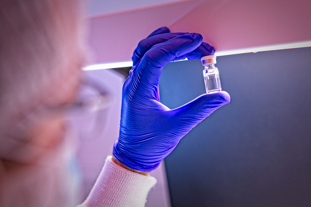 Gmp biologics manufacturing scientist holding a vial of drug product up to the light for visual inspection