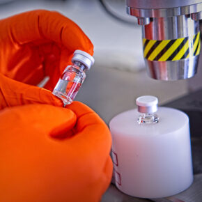 Symbiosis scientist's hand holding vial on front of crimping and capping equipment